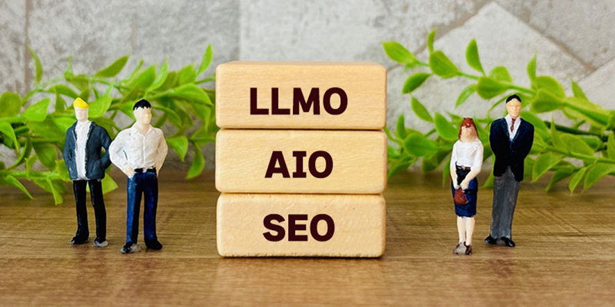 LLMO、AIO、SEOと書かれた木製ブロックの周りに立つビジネスマンとビジネスウーマンの人形